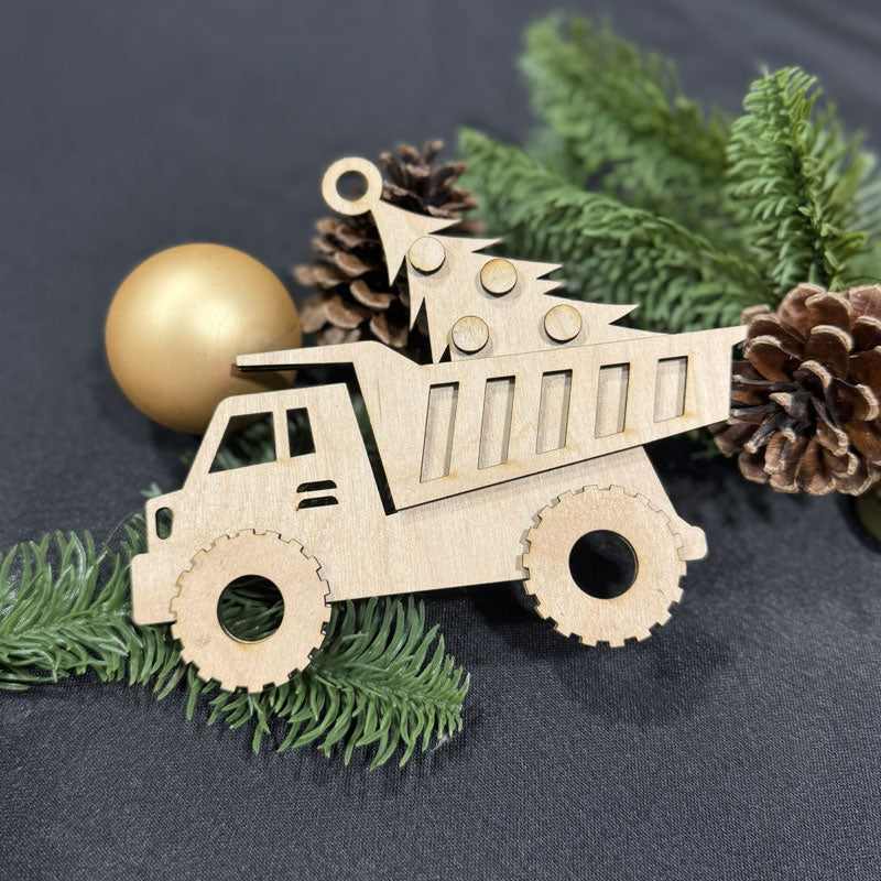 Wooden dump truck ornament on a dark surface with greenery and pine cones.