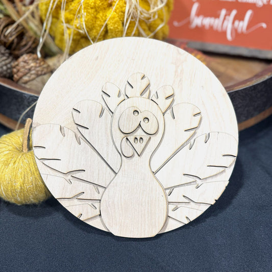 Wooden googly eyed turkey sign with fall decorations in the background.