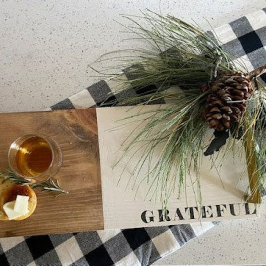 Wooden tray with glass, bread, and butter on a checkered tablecloth with 'GRATEFUL' sign.