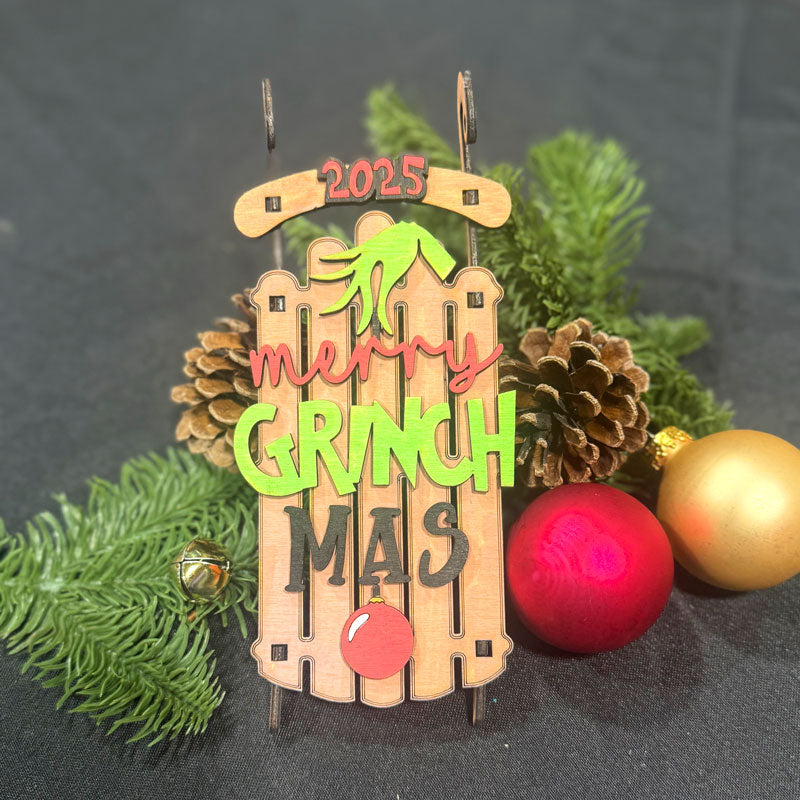Decorative ornament with 'Merry Grinch Mas' text and festive decorations on a dark background