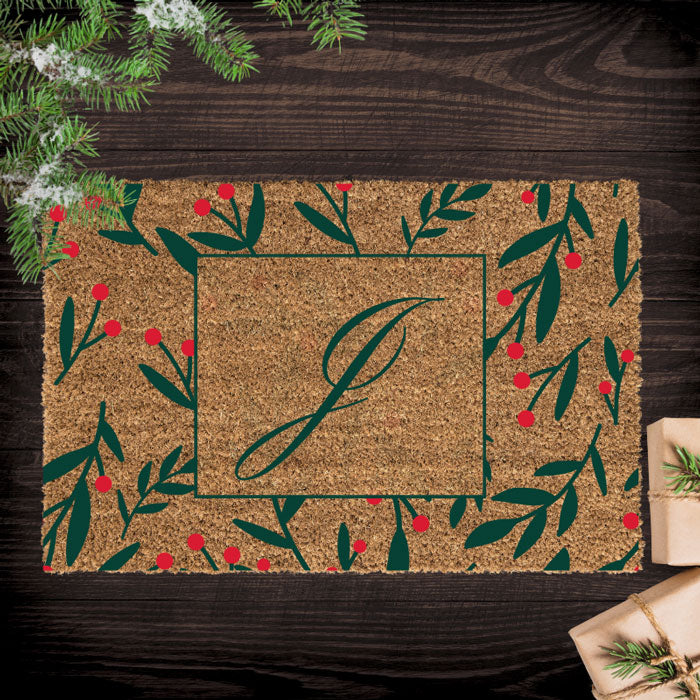 Decorative doormat with a monogram on a wooden surface with Christmas decorations.
