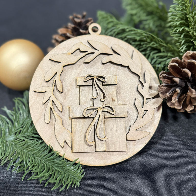 Wooden Christmas ornament with gift design surrounded by greenery and pine cones on a dark surface