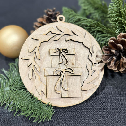 Wooden Christmas ornament with gift design surrounded by greenery and pine cones on a dark surface