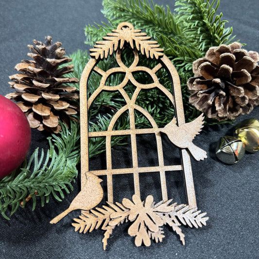 Decorative Christmas ornament with birds and a window on a dark background with pine cones and a red ball.