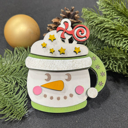 Decorative snowman mug with a candy cane hat on a dark background with greenery.