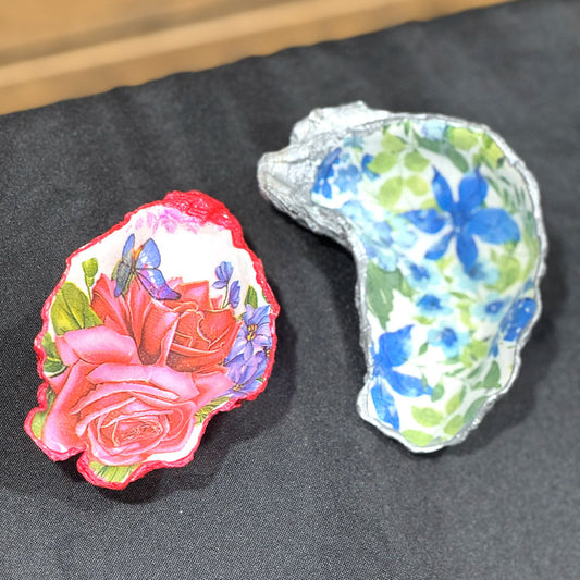 Two decorative oyster shells with floral designs on a dark surface.