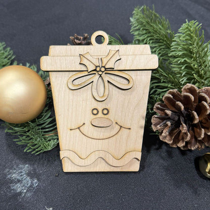Wooden reindeer ornament with a bow on a dark background with greenery and pine cones.