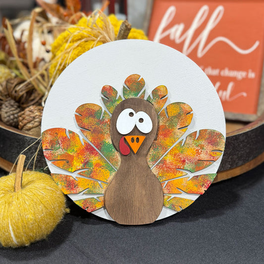 Adorable googly eyed turkey with multicolored feathers with fall decorations in the background.