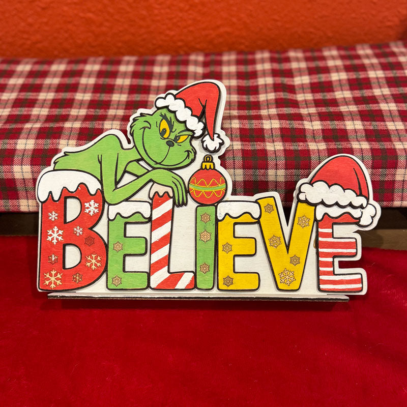 Decorative sign with 'Grinch' character and 'BELIEVE' text on a red background