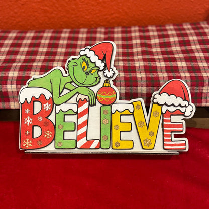 Decorative sign with 'Grinch' character and 'BELIEVE' text on a red background