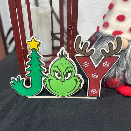 Christmas-themed decorative letters spelling 'JOY' with a Grinch face and tree design.