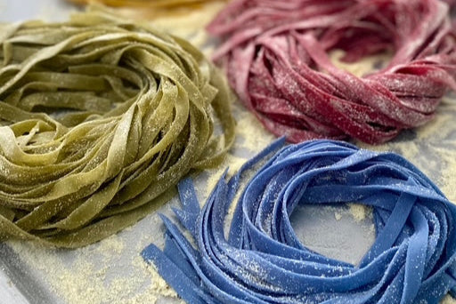 Three nests of colorful pasta on a baking sheet.