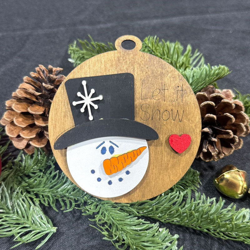 Wooden ornament with snowman design, pine cones, and greenery on a dark background