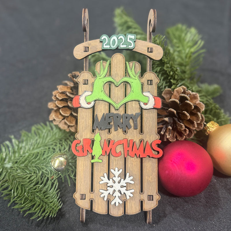 Decorative Christmas ornament with 'Merry Grinchmas' text and festive elements on a dark background.