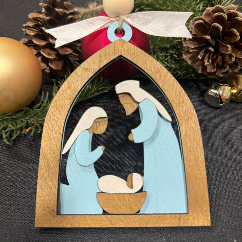Decorative nativity scene ornament with wooden frame and Christmas decorations in the background.