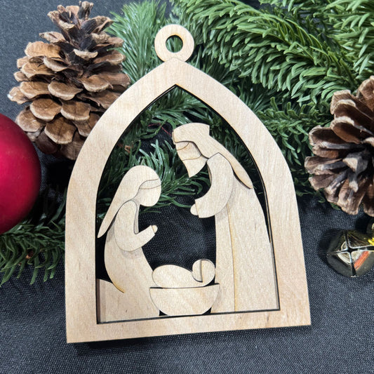 Wooden nativity scene ornament with pine cones and greenery on a dark background