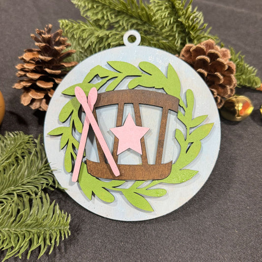 Decorative Christmas ornament with a star and pink ribbon on a gray background with greenery and pinecones.