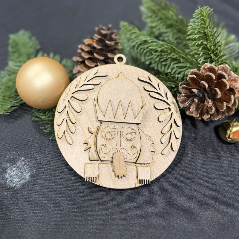 Wooden Christmas ornament with a design on a dark surface with greenery and pine cones.