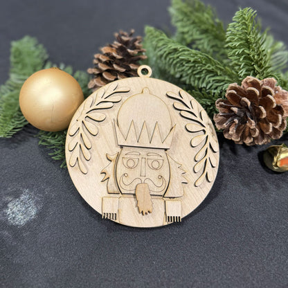 Wooden Christmas ornament with a design on a dark surface with greenery and pine cones.