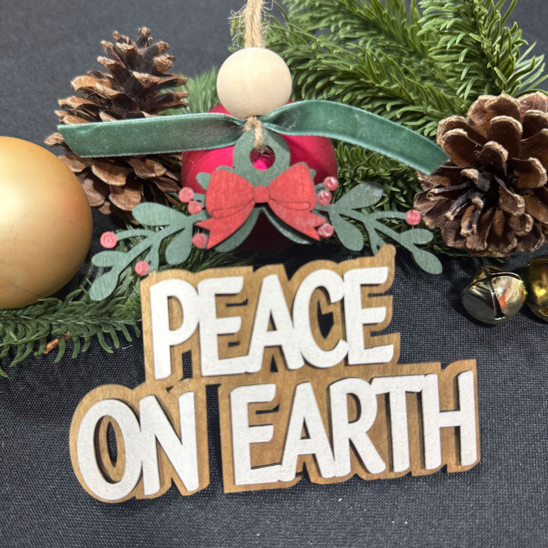 Christmas ornament with 'Peace on Earth' text surrounded by greenery, pinecones, and a red bow.