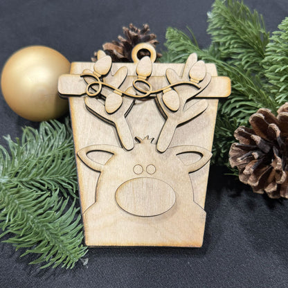 Wooden reindeer ornament on a dark background with greenery and pine cones.