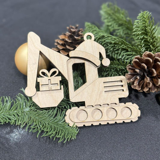 Wooden excavator ornament with a Santa hat on a dark surface with greenery and pine cones.