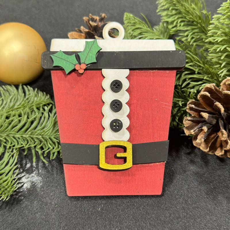 Red cup-shaped Christmas ornament with buttons and holly leaves on a dark background with greenery.