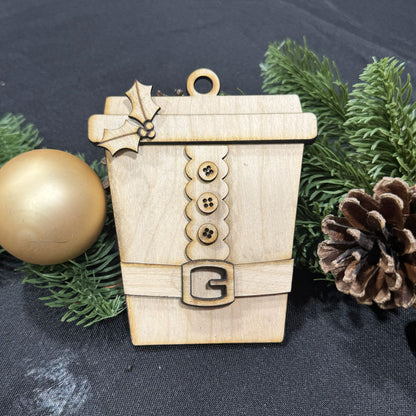 Wooden ornament shaped like a coffee cup with decorative elements on a dark fabric background.