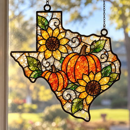 A stained-glass-style Texas-shaped hanging suncatcher with orange pumpkins, yellow sunflowers, green leaves, and black metal outlines, displayed in front of a window with a blurred outdoor background.