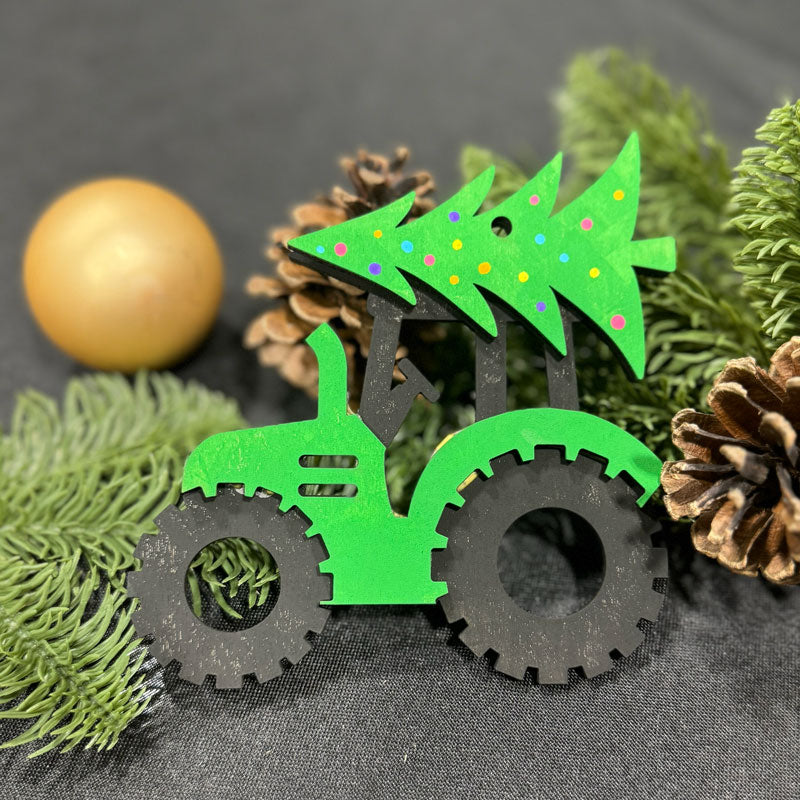 Green toy tractor ornament with a Christmas tree on a gray background with pine cones and a ball.