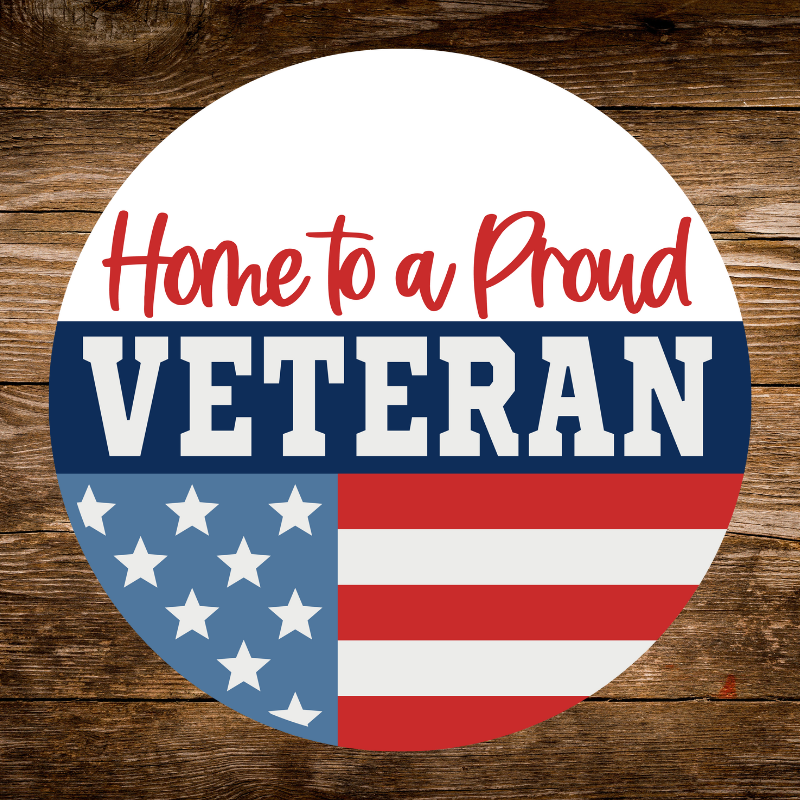 Round Sign with 'Home to a Proud Veteran' text on an American flag background, placed on a wooden surface.