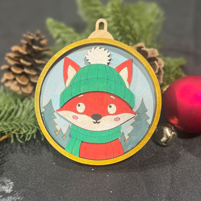Decorative fox ornament with a green hat and red scarf on a dark background with pine cones and a red ball.
