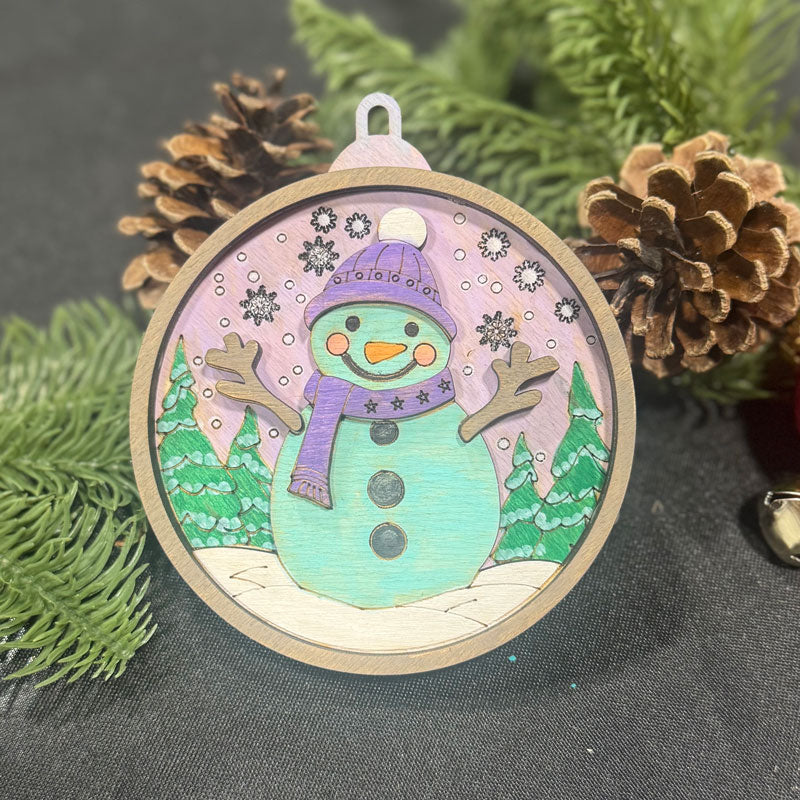 Decorative snowman ornament with a purple hat and scarf, surrounded by pine cones and branches.